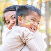 Thumbnail for child with fall tattoo on his cheek outside with his mother